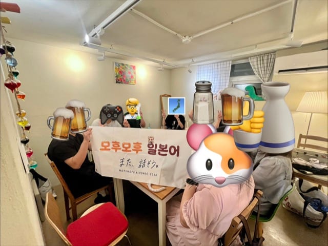 수다회 56회차 참가자들이 얼굴을 가리고 모후모후 일본어 현수막과 함께 찍은 단체 사진